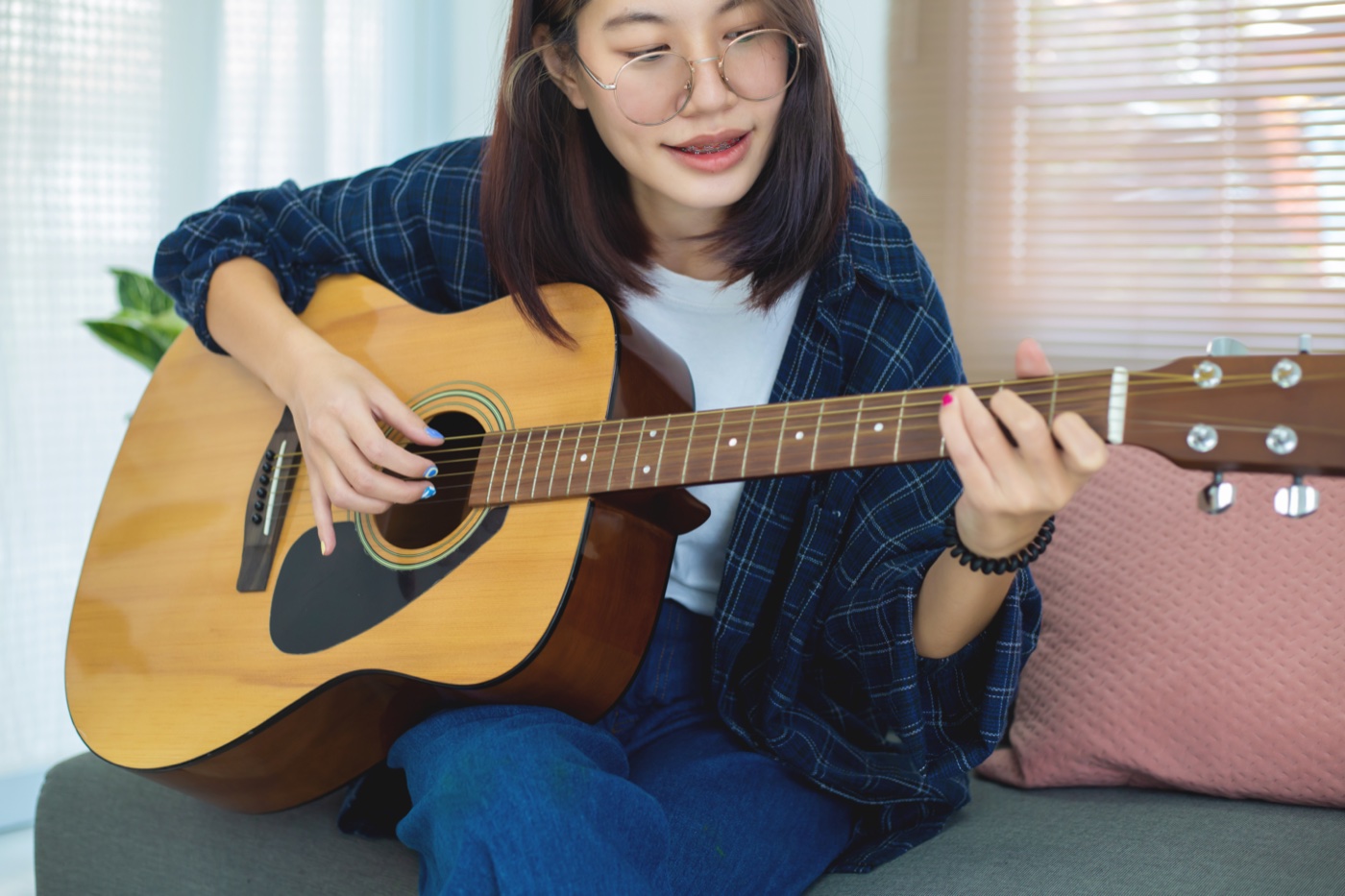 ソファでアコースティックギターの弾き語りを練習する女性